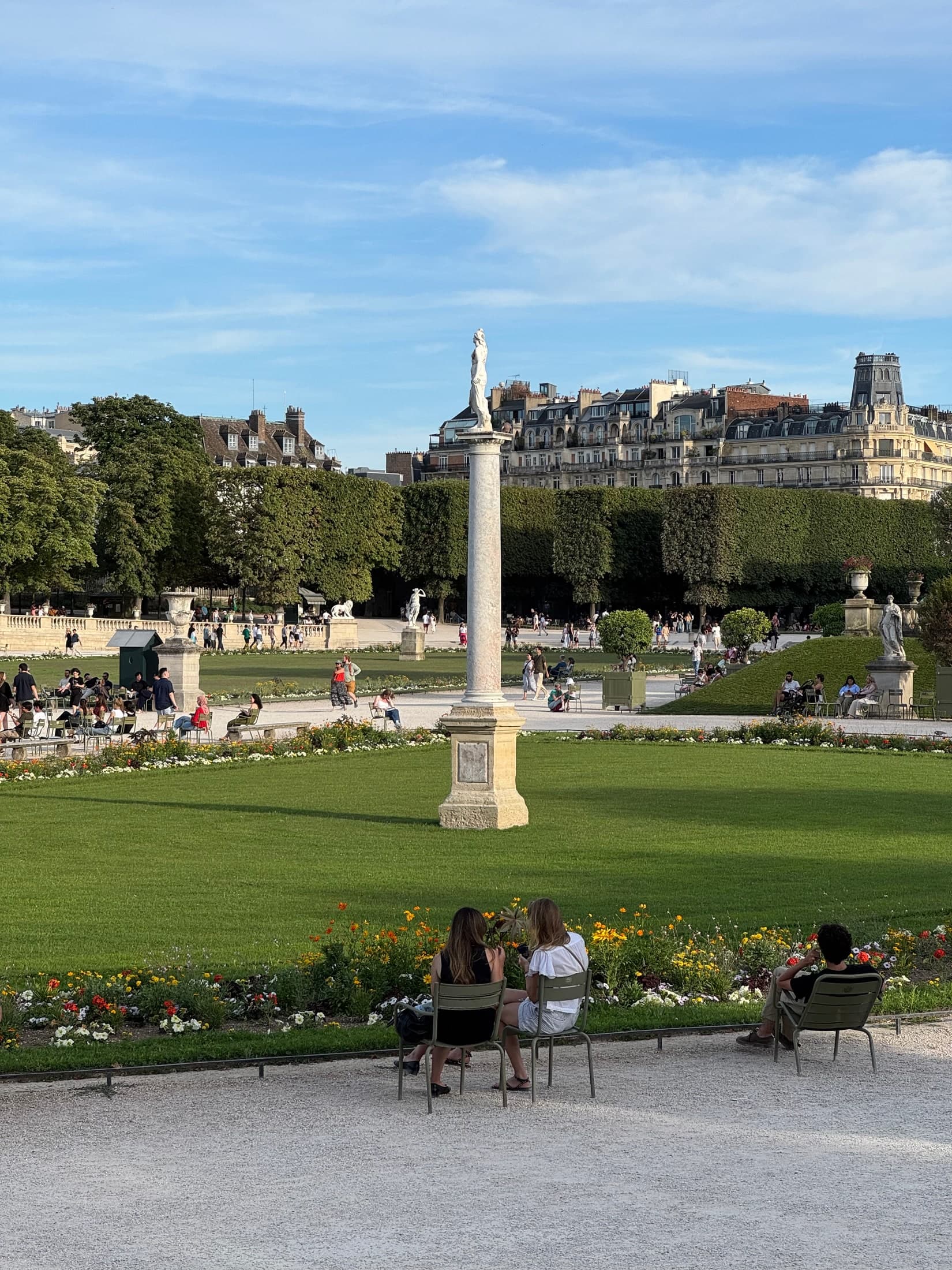 Pelouse centrale et colonne du Jardin du Luxembourg, avec des visiteurs assis sur les chaises vertes