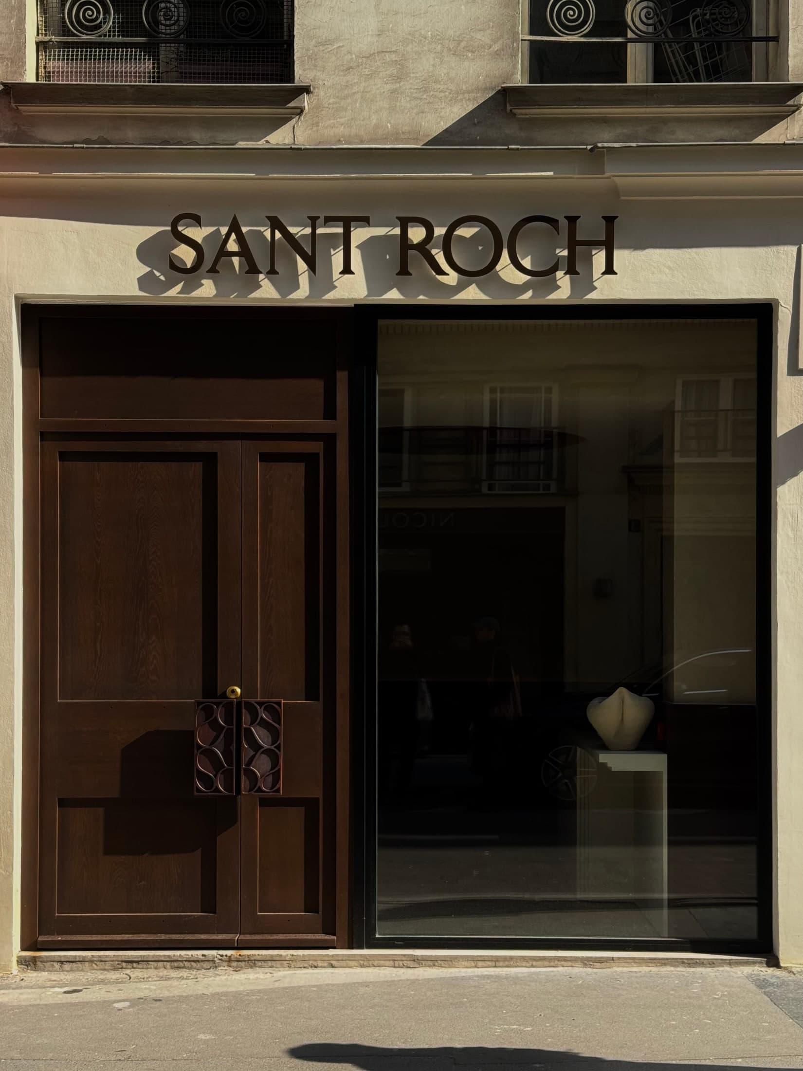 Enseigne SANT ROCH au soleil, au-dessus d’une porte en bois sombre à Paris